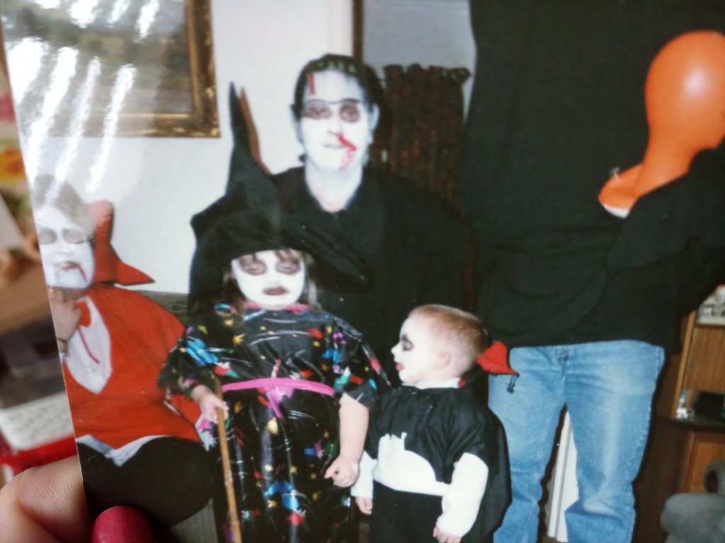 Image shows a family dressed up for Halloween in the mid-1990s. One is a vampire, one Frankenstein's creature, another a headless man. Two children in the front are dressed as a witch and a vampire.